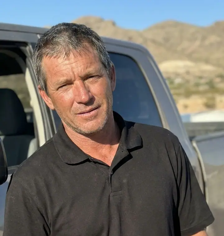 Daniel Smith, manager of Lifetime Roofing of El Paso, in a black polo beside a dusty pickup with desert hills behind him