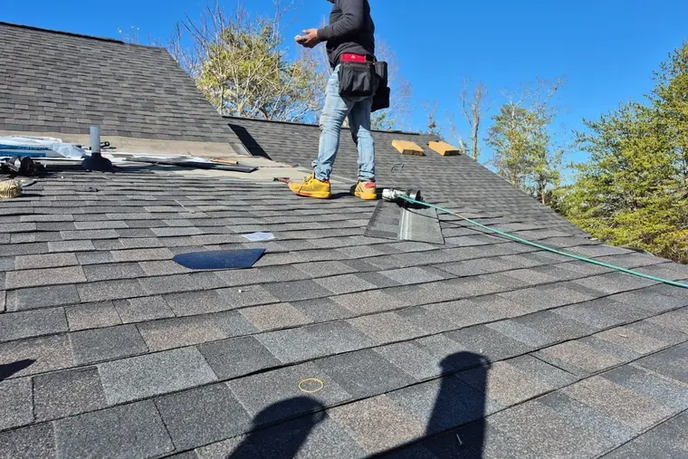 Roofer standing on a gray shingle roof under a blue sky
