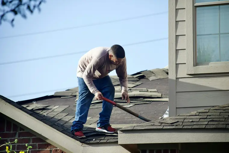 Roofer prying up shingles on a house roof