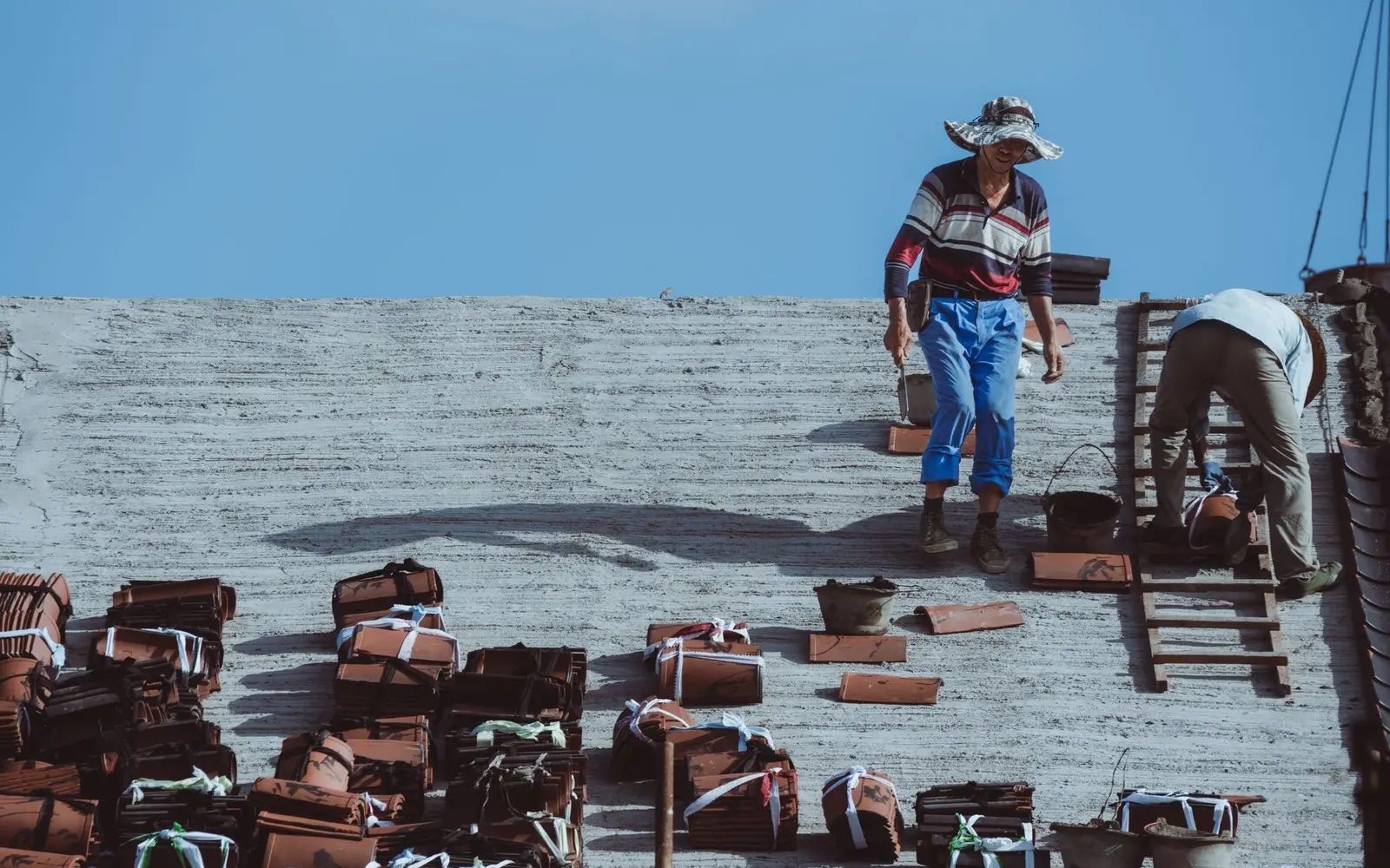 Roofers working among stacked clay tiles on an open roof