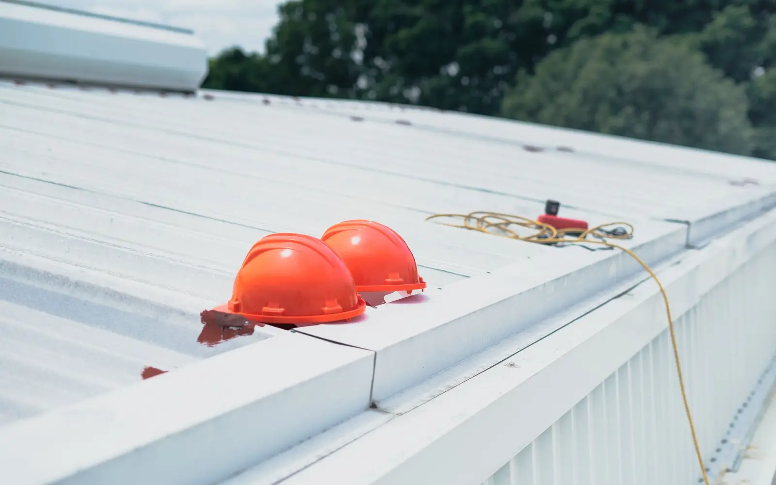 Two hard hats resting on a white commercial metal roof
